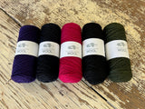 Five balls of Kangaroo Island Wool yarn in iris, navy, impressa, and olive on a wooden surface.